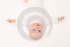 Cute baby girl in a white bodysuit on a white isolated background looking at the camera, baby 3 months old lying on the bed upside