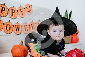 Cute baby girl in witch halloween costume at home, sitting on bed with Halloween decoration, Lifestyle indoors