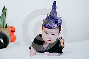 Cute baby girl in witch halloween costume at home, sitting on bed with Halloween decoration, Lifestyle indoors