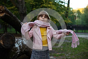 Cute baby girl wraps up in a pink scarf in an autumn Park and plots to play pranks photo