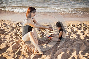 Cute baby girls playing with sand on the beach, and mom gently looking at her daughter.