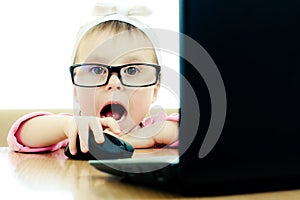 Cute baby with glasses looking into the laptop