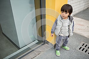 Cute baby in gray suit and green shoes standing and posing in front of glass door