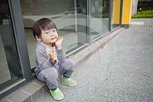 Cute baby in gray suit and green shoes standing and posing in front of glass door