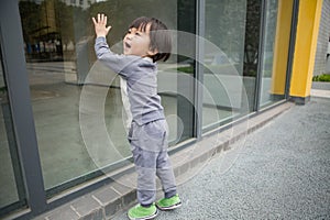 Cute baby in gray suit and green shoes standing and posing in front of glass door