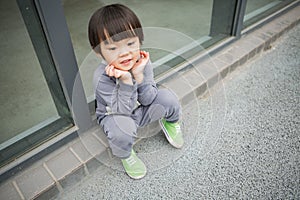 Cute baby in gray suit and green shoes standing and posing in front of glass door