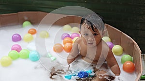 Cute baby having fun taking bath playing in water with foam with colorful toys.