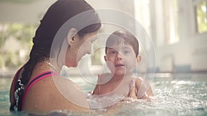 Cute baby having swimming lesson with his mother. Mother teaching her son to swim in the swimming pool. Young mom takes