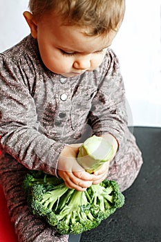 Cute baby holding broccoli in his hands, sitting on the floor indoors