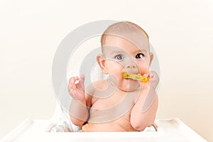 Cute baby infant kid biting sitting in highchair and chewing yellow eething toy copy space bright minimal healthcare