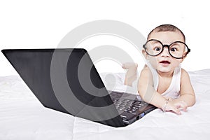 Cute baby with laptop and glasses on bed