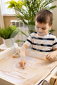 Cute baby little boy drawing smiley fun face on sand table therapy fine motor skills top view