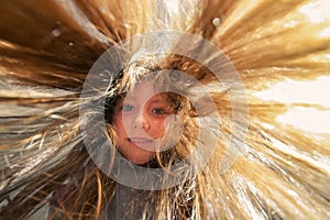 A cute baby with long hair looks down. Children`s portrait wide-angle photo. Portrait of a cheerful little girl with her hair