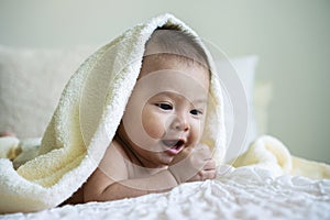 cute baby looking at camera under white blanket. Innocence baby crawling on white bed with towel on his head at home