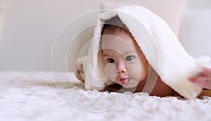 Cute baby looking at camera under white blanket looking at something. Innocence baby crawling on white bed with towel on