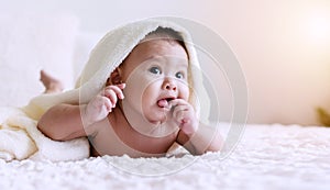 Cute baby looking at camera under white blanket looking at something. Innocence baby crawling on white bed with towel on