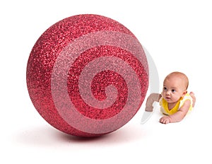 Cute Baby looking at a Huge Christmas Ornament on white