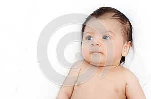 Cute baby is looking up to someone on white bed