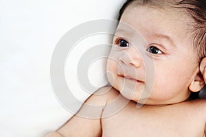 Cute baby is looking up to someone on white bed