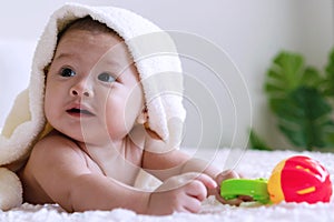 Cute baby lying on bed with toy under white blanket looking at something. Innocence baby crawling on white bed with towel