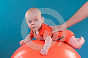 Cute baby lying on the orange fitball on the blue background. Co