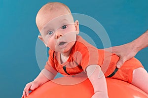 Cute baby lying on the orange fitball on the blue background. Co