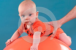 Cute baby lying on the orange fitball on the blue background. Co