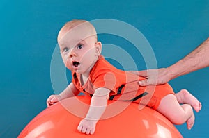 Cute baby lying on the orange fitball on the blue background. Co