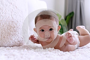 Cute baby lying and relax on white bed looking at camera. Newborn boy wear diapers playing on the bed at home