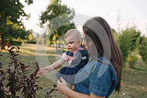 Cute baby on mom`s hands outside. Family in the park in summer. Denim style. Mom and daughter in jeans