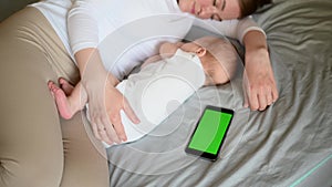 Cute baby and mother hugging sleep at home in bed next to phone, color key. Child safety and protection, co-sleeping