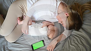 Cute baby and mother hugging sleep at home in bed next to phone, color key. Child safety and protection, co-sleeping