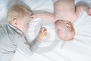 Cute baby and older brother interact while lying on the bed. Top view