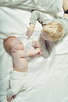 Cute baby and older brother interact while lying on the bed. Top view