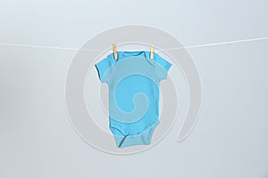 Cute baby onesie hanging on clothes line against light grey background