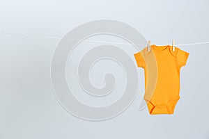 Cute baby onesie hanging on clothes line against light grey background. Laundry day