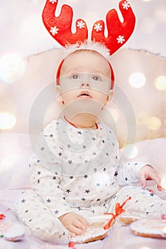 Cute baby in pajamas and deer horns on christmas background