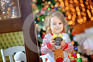 Cute baby in pajamas plays with a clock in a festively decorated room