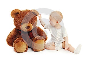 Cute baby playing with big teddy bear on white