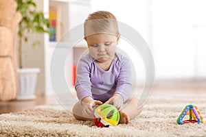 Cute baby playing with colorful toys sitting on carpet in white sunny bedroom. Child with educational toy. Early
