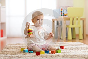 Cute baby playing with colorful toys sitting on carpet in white sunny bedroom. Child with educational toys. Early