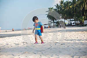 Cute baby in red cape poses as superman on the beach