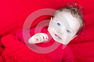 Cute baby in red sweater under red blanket