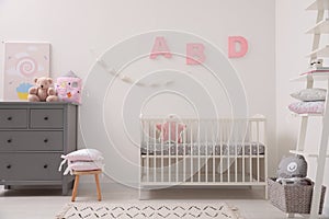 Cute baby room with crib and chest of drawers near white wall