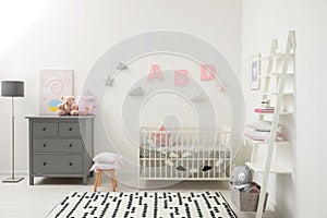 Cute baby room interior with crib and chest of drawers near white wall