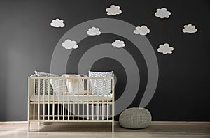 Cute baby room interior with modern crib near decorative clouds on wall