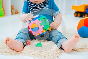 cute baby is sitting on the floor of the house, playing with colorful educational toys