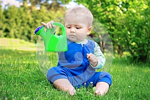 Cute baby sitting on the grass in park with watering can