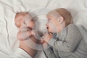 Cute baby and smiling older brother are lying on the bed. Play and interact. Top view