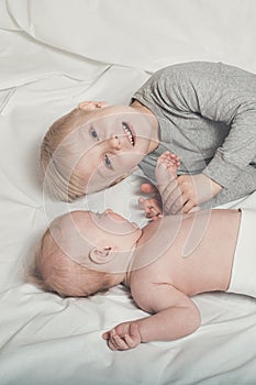 Cute baby and smiling older brother are lying on the bed. Play and interact. Top view